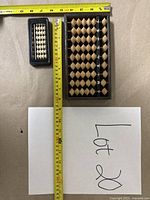 Two Asian counting devices including one smaller and one larger abacus pictured with measuring tape for size reference.