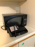 Danby black countertop microwave placed on a kitchen counter with the power cord visible, showing keypad and door.