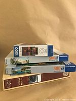 Stack of four puzzle boxes: John Bradly 1000-piece, two Ravensburger 500-piece puzzles, and a Cobble Hill 1000+ piece puzzle