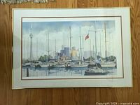 Framed print showing Toronto harbour with multiple sailboats and the downtown skyline featuring the CN Tower, mounted on a hardwood floor for scale.