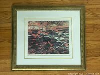 Front view of framed print showing red maple leaves over river with cream double mat and gilt frame on wood floor
