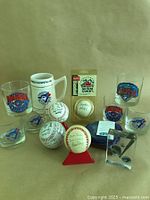 Full lot showing nine commemorative glasses and tankard with various Blue Jays 1992 and All-Star logos, six baseballs including autographed ones, and an acrylic Blue Jays logo piece.