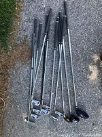 Overhead shot of all golf clubs on asphalt, showing irons, woods, and putter.