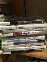 Stack of 8 Xbox 360 game cases showing titles from Dishonored, NHL 13, Batman Arkham, Assassin's Creed series, to Skyrim