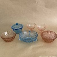 All six pieces of the depression glass set shown together, displaying pink and blue colors with different shapes and patterns
