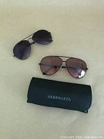 Two aviator sunglasses laid flat with Serengeti branded soft case
