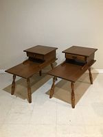 Two brown mid-century end tables side by side, showing rectangular tops with raised drawer compartments and turned legs.
