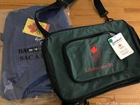 Photo showing the green Lillehammer 94 souvenir shoulder bag with front pocket and attached official Samboro tag. The blue Sydney 2000 bag is visible in packaging behind it.