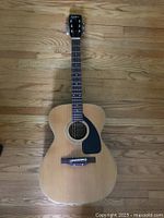 Full front view of natural wood finish acoustic guitar with black pickguard and six strings.