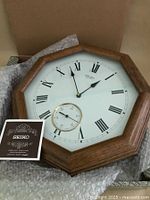 Octagonal Seiko wall clock face showing Roman numerals and seconds dial, with original Seiko paper included beside it.