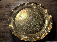 Top angled view of the antique Chinese brass plate showing scalloped edges and detailed dragon etching in the center surrounded by floral patterns.