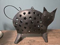 Front view of large iron cat-shaped lantern candle holder showing star-shaped cutouts and handle.