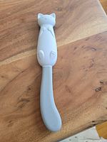 Front view of the cat shaped jar scraper on a wood surface showing the detailed cat design on handle and silicone blade.