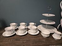 Full display of the tea set showing six cups and saucers, the open sugar bowl, creamer, and the three-tiered dessert stand arranged on a wooden surface.