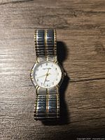 Full view of vintage Sergio Valente men's wristwatch, showing two-tone stainless steel and gold-tone elasticized band and round white dial with gold hands and black Arabic numerals.