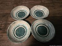 Four handmade ceramic dishes with blue circular patterns viewed from above on a wooden surface.