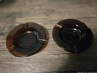 Pair of brown glass ashtrays side by side on a wooden surface, showing size and color difference.