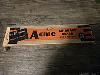 Original box for Acme cribbage board, orange with black text, showing worn and torn ends