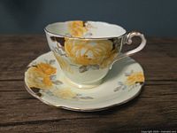 Close-up front angle of vintage Aynsley teacup with yellow rose design and matching saucer on wooden surface
