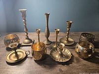 Overview of 11 brass candlesticks and tealight holders on wooden surface, various styles and patterns, natural brass tone, some with star cutout decorations.
