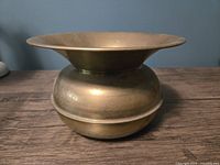 Front side view showing rounded base and wide flared top opening of the brass vase