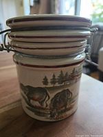 Side view of ceramic canister showing horse and cow illustrations with cream base and maroon trim, metal hinge locking lid visible.