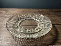 Photo showing top view of the clear hobnail glass ashtray with round shape and raised knob texture along the rim and multiple cigarette slots around the central ash area.