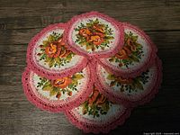 Six round doilies/coasters stacked, showing floral pattern with pink crochet border