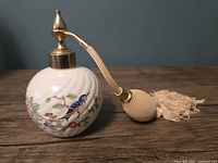 Side view showing the porcelain bottle with colorful bird and floral designs, gold spray top, woven bulb and tassel attached.
