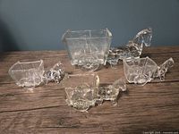 Five clear pressed glass horse and buggy candy dishes or planters on wooden surface: one large and four smaller pieces showing full lot.