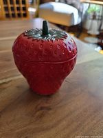 Strawberry-shaped sugar bowl closed, showing red textured exterior and green painted lid.