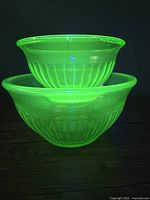 Two bowls stacked inside each other glowing bright yellow-green under black light showing ribbed optic glass pattern.
