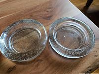 Two round clear bubble glass dishes placed on a wooden surface, showing top view and bubble texture inside the glass.