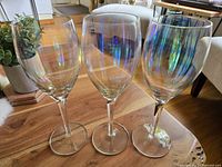 Three vintage iridescent wine glasses arranged side-by-side on wooden surface. The glasses display a rainbow-like iridescent effect on the bowl portion with clear stems and bases.