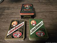 Two decks of playing cards, one green and one black, both with Jack Daniel's Old No. 7 branding and portrait