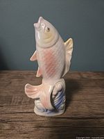 Front and side view of vintage lustreware fish sculpture showing pink and yellow pastel tones and detailed textured scales on base mimicking waves.