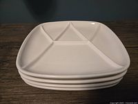 Stack of 4 white multisectioned plates shown from the side angle.