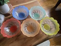 Top view showing five vintage small glass bowls by Pasari Indonesia in blue, pale green, coral red, peach, and yellow colors with scalloped edges.