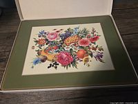 Set of four vintage Pimpernel placemats with floral and fruit basket illustration, green border and cork backs, displayed inside open box.