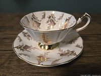 Photo of vintage Queen Anne teacup and saucer featuring Scottish Thistle design with gold accents, shown on wooden surface.