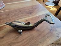 Vintage silver plated dolphin-shaped bottle opener lying on wooden surface showing its full form and metallic patina.