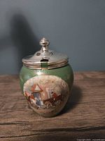 Front view of vintage William Wood & Co. Staffordshire pottery jam pot featuring a green glaze and a transfer print of a hunting party arriving at a house. The silver-plated lid has a spoon notch and finial knob.