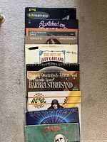 Collection of 9 vinyl records stacked with visible titles including Greg Kihn, Barbra Streisand, Kristofferson, Judy Garland, Queen, AC/DC, Journey.