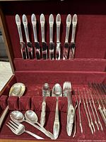 Flatware utensils arranged in a red velvet lined compartmentalized case with visible knives, forks, spoons and serving utensils from 1847 Rogers Bros sets