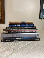 Stack of nine books showing titles and spine details, including Women of Windsor, Art Nouveau, Buckingham Palace history, Burnaby, Joan Rivers Jewelry, Cartier, drawing dragons, and great palaces.