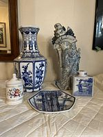 Photo showing all five porcelain items: tall vase, jester figurine, tea caddy, hexagonal plate, and lidded jar arranged on a quilted surface in front of a mirror
