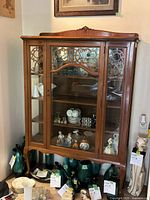 Front view of the mahogany curio cabinet showing three glass display shelves behind decorative glass doors with intricate circular designs, curved top edge with carved crest.