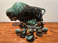 Buffalo figurine with two roosters and a duck in front on wooden surface against a plain white wall, showing overall set and detail of glaze.