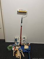 Full spread of painting accessories including rollers on pole, paint roller covers, paint brushes, sanding sheets, tape, scraper, and tarp.