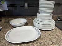 Overall view of dinnerware set including stacked plates, bowls, and cups with a large serving platter in front